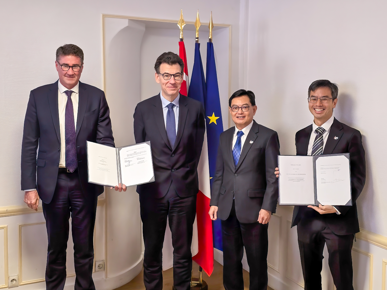 Four men in suits holding documents stand before flags of France and Vietnam.